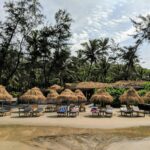 Relaxing beachside view with nipa huts and palm trees in Goa, India, perfect for a tropical getaway.
