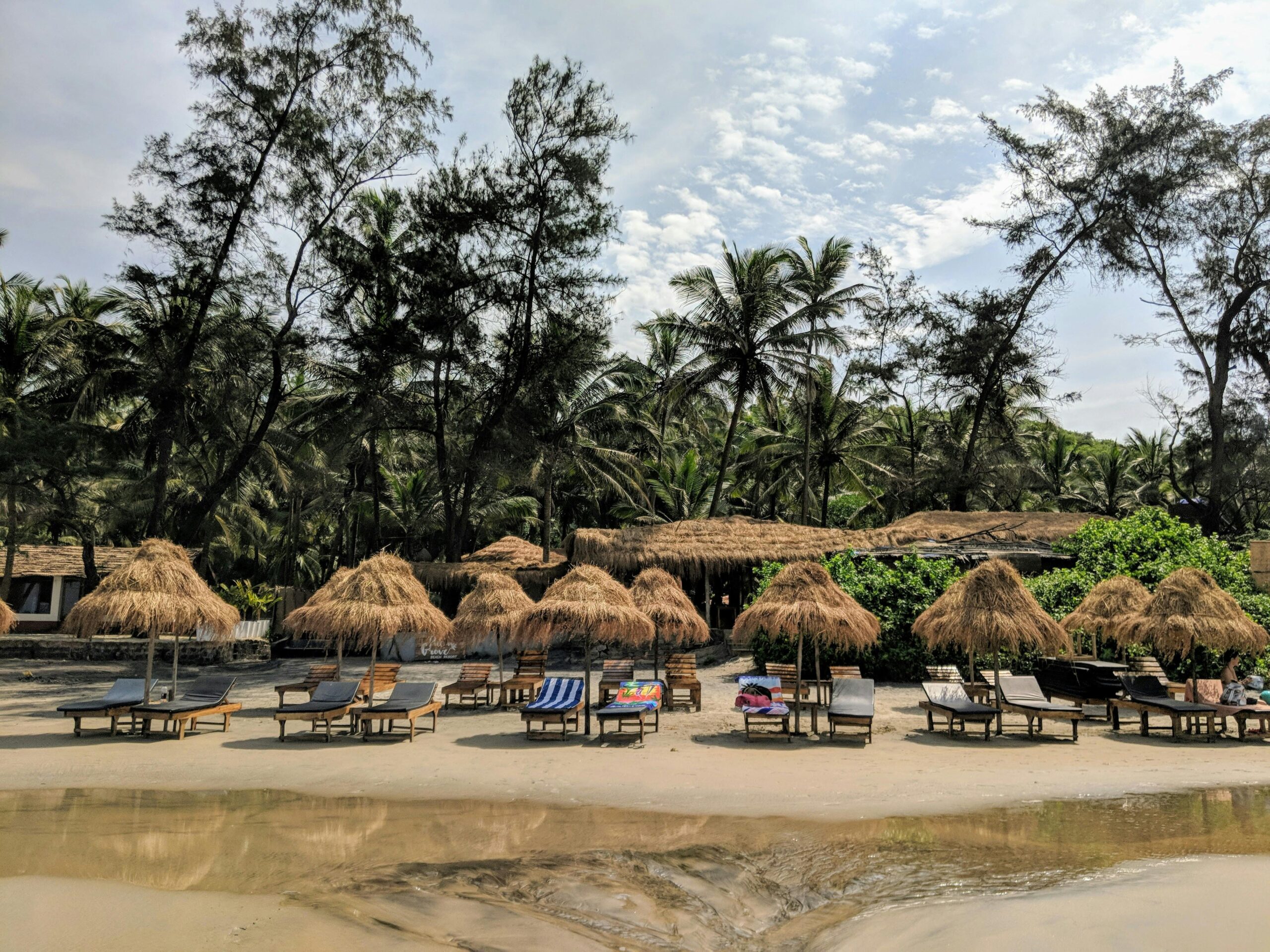 Relaxing beachside view with nipa huts and palm trees in Goa, India, perfect for a tropical getaway.
